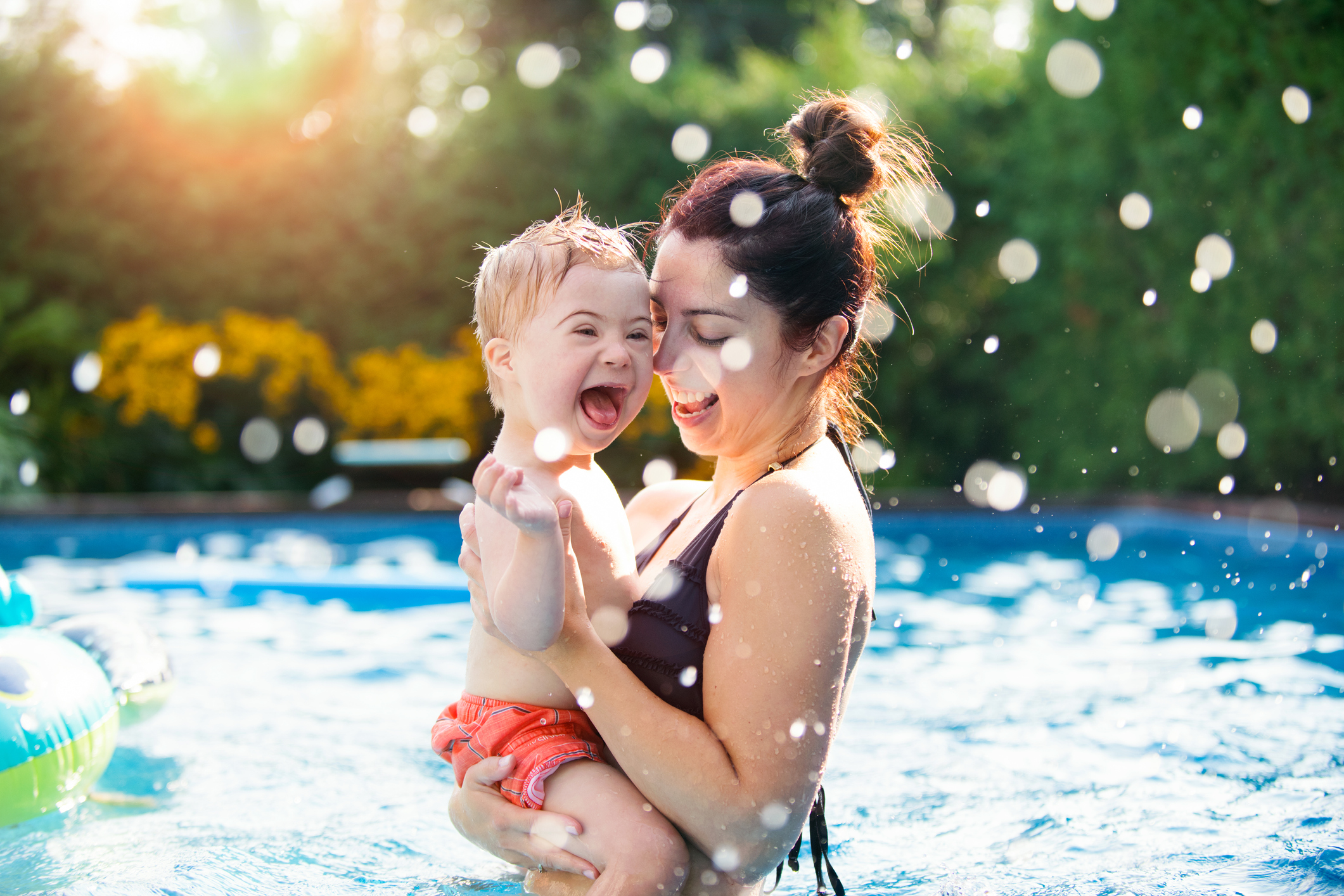 Little boy with Down syndrome having fun in the swimming pool with his family